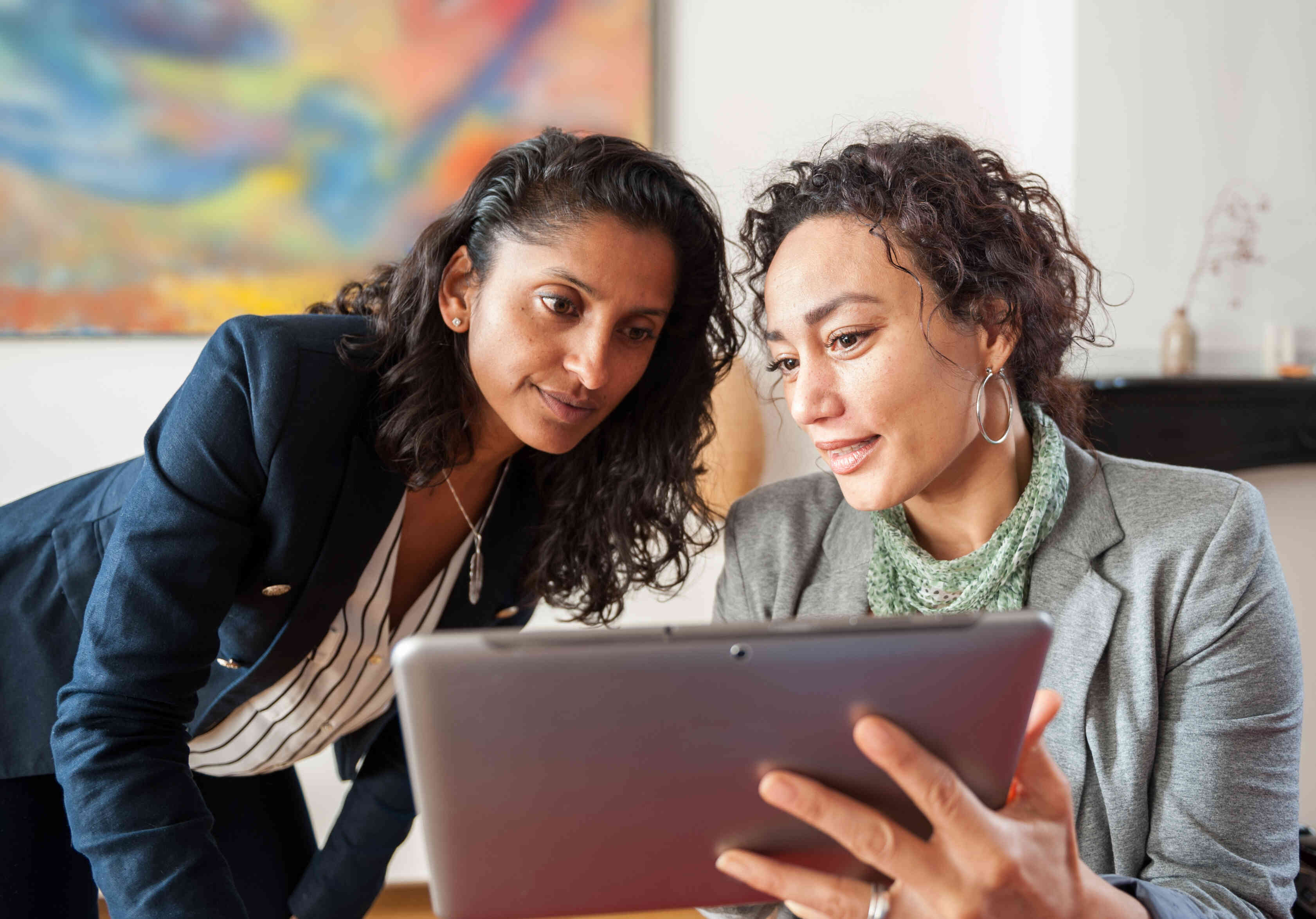 Two woman are looking at a tablet, appearing to discuss something.